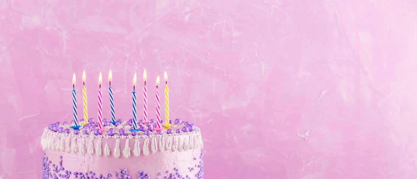 Birthday cake with purple sprinkles and colorful candles over pink background